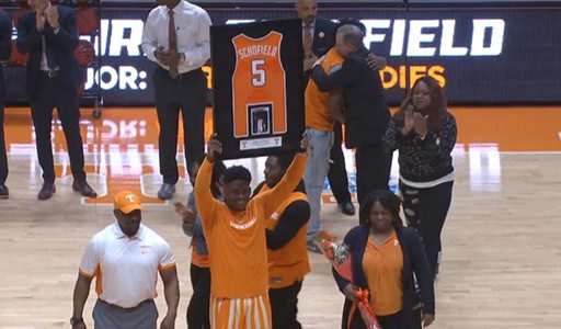 Basketball player holding framed jersey on court.