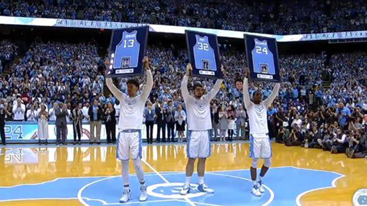 Three basketball players holding framed jerseys.