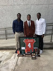 Three men standing with sports memorabilia display.