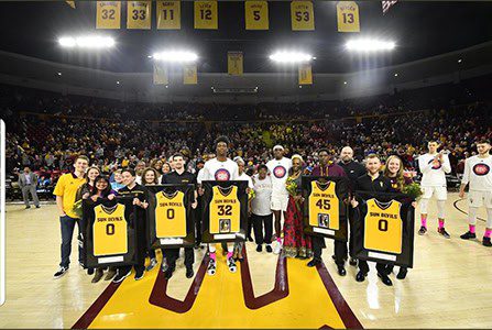 Basketball team holding jerseys on court.